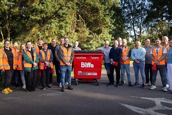 Group of volunteers from local businesses and community picking litter from woodland