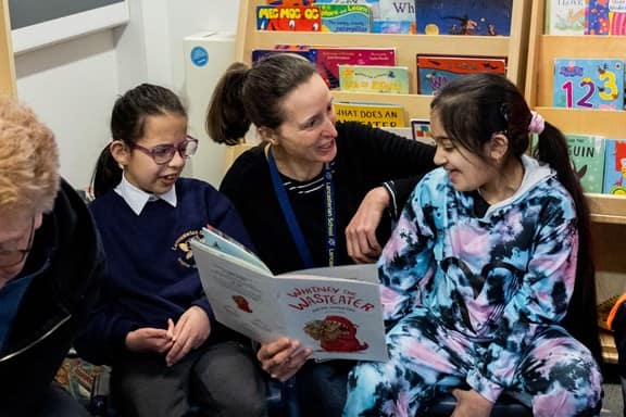 Teacher reading storybook to 2 students