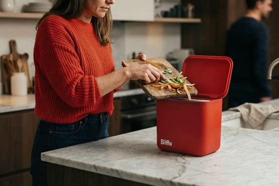 Women scrapping food into red kitchen caddy