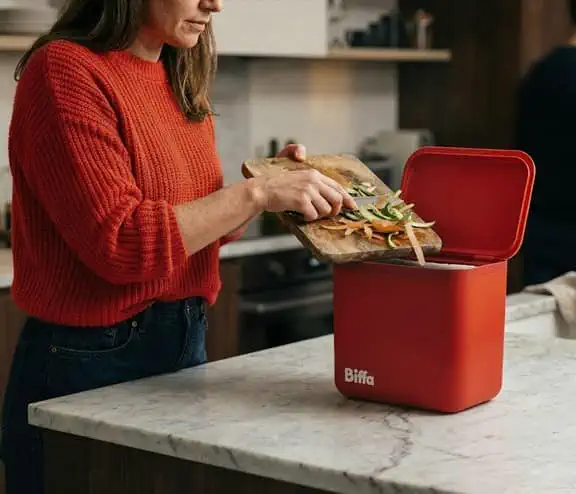 Women scrapping food into red kitchen caddy