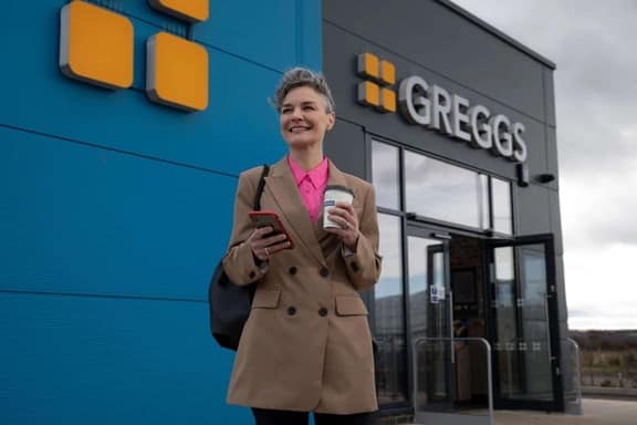 Person with coffee in front of Greggs store