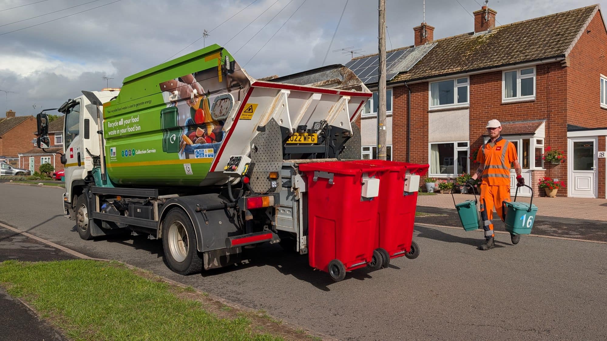 Bin lorry being operated by employee emptying red smart bins