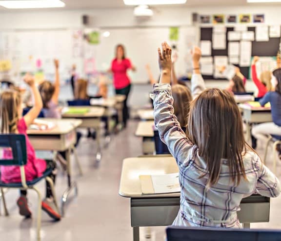 Children in classroom with hands raised
