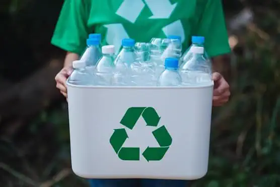 A woman collecting garbage and holding a recycle bin with plastic bottles in the outdoors