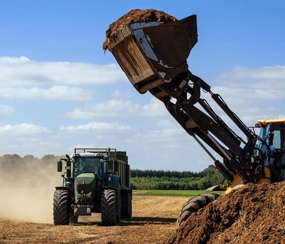 excavator with a shovel full of organic fertilizer ready to fill the trailer of a tractor